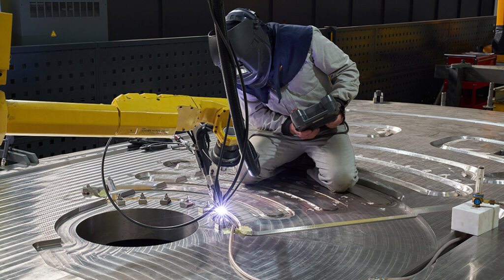 Operario de Asturfeito trabajando en una célula de soldadura robotizada de acero inoxidable