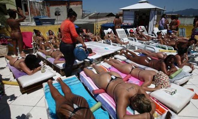 Ariba, mujeres tomando el sol. Abajo una mujer pega las tiras adhesivas que simulan un bikini en una terraza en Río de Janeiro (Brasil). 